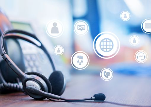 A headset propped up next to a phone with some icons demonstrating various digital technology 