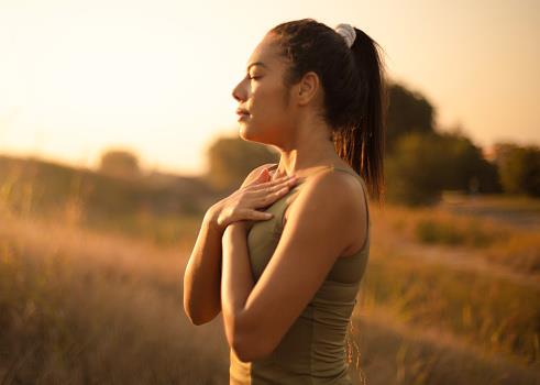 A woman stood in a field with her eyes closed and her arms crossed over her chest.