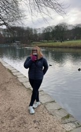 A person wearing a navy blue coat and white trainers stood next to a river of water.