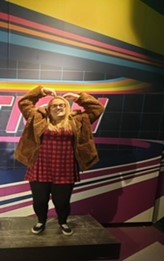 A person in a brown fur coat with her fingers pointing on top of her head.