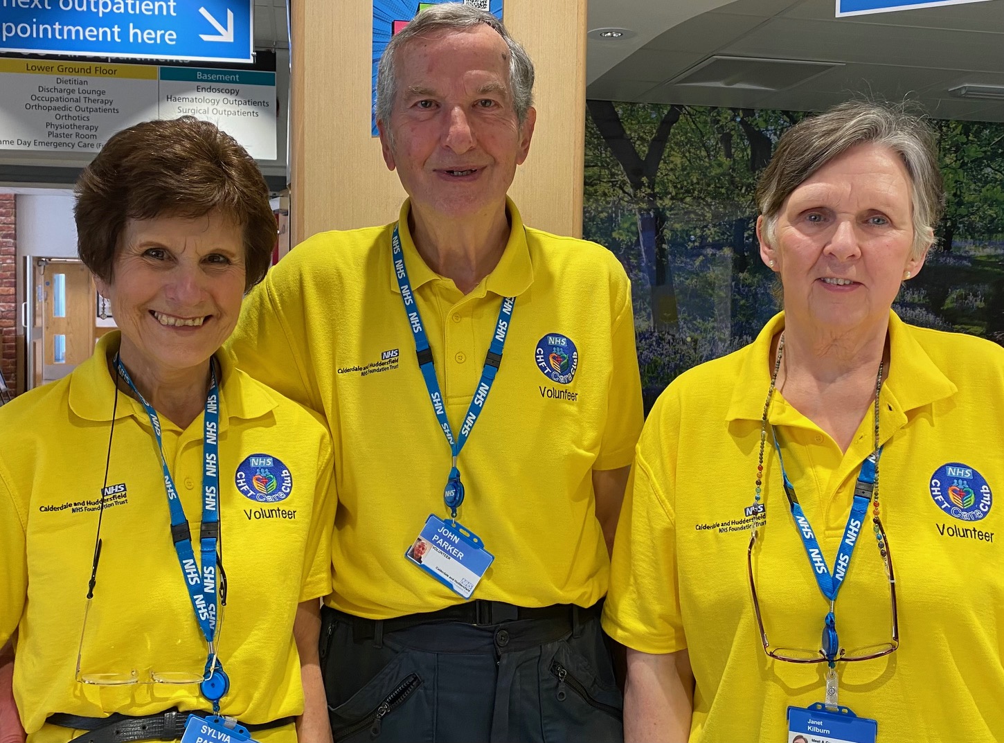A group of 3 people all wearing yellow Volunteer polo shirts with NHS lanyards on.