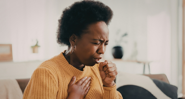 A black woman in a mustard jumper coughing
