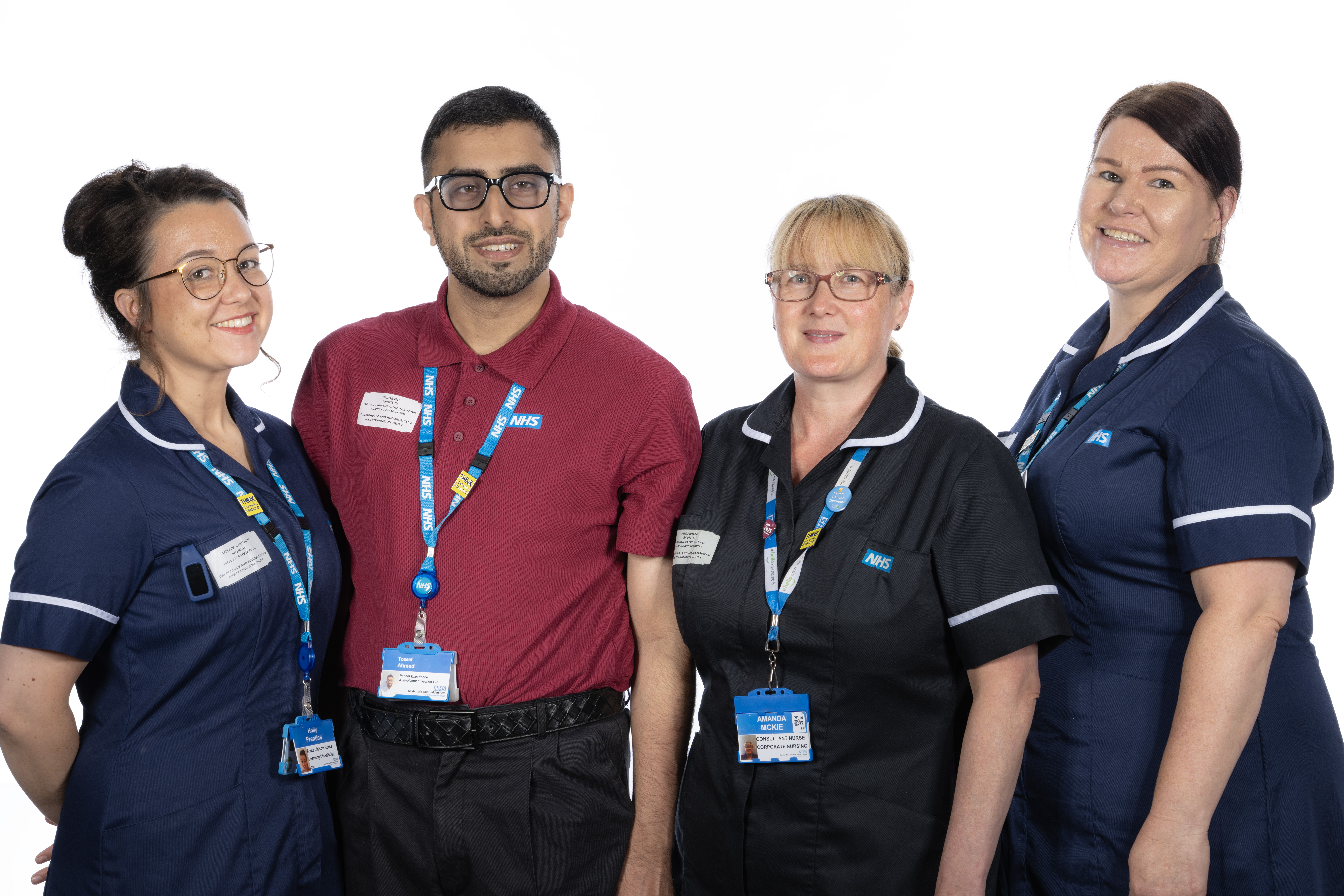 Three women and one man stood smiling in front of a white background