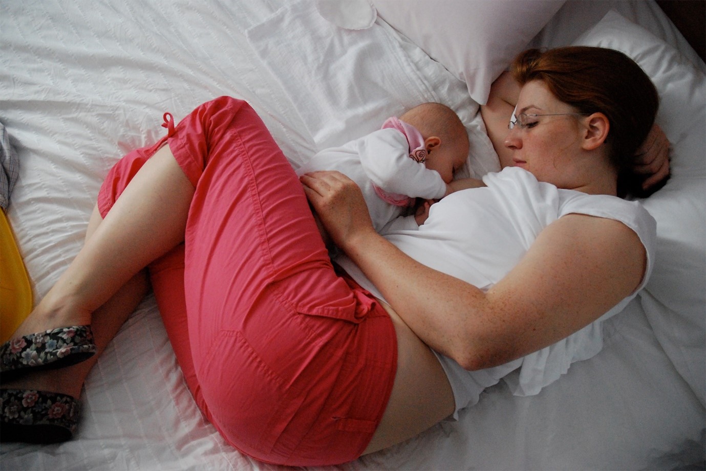 Mother and baby laying on their side facing each other in a breastfeeding position on a bed