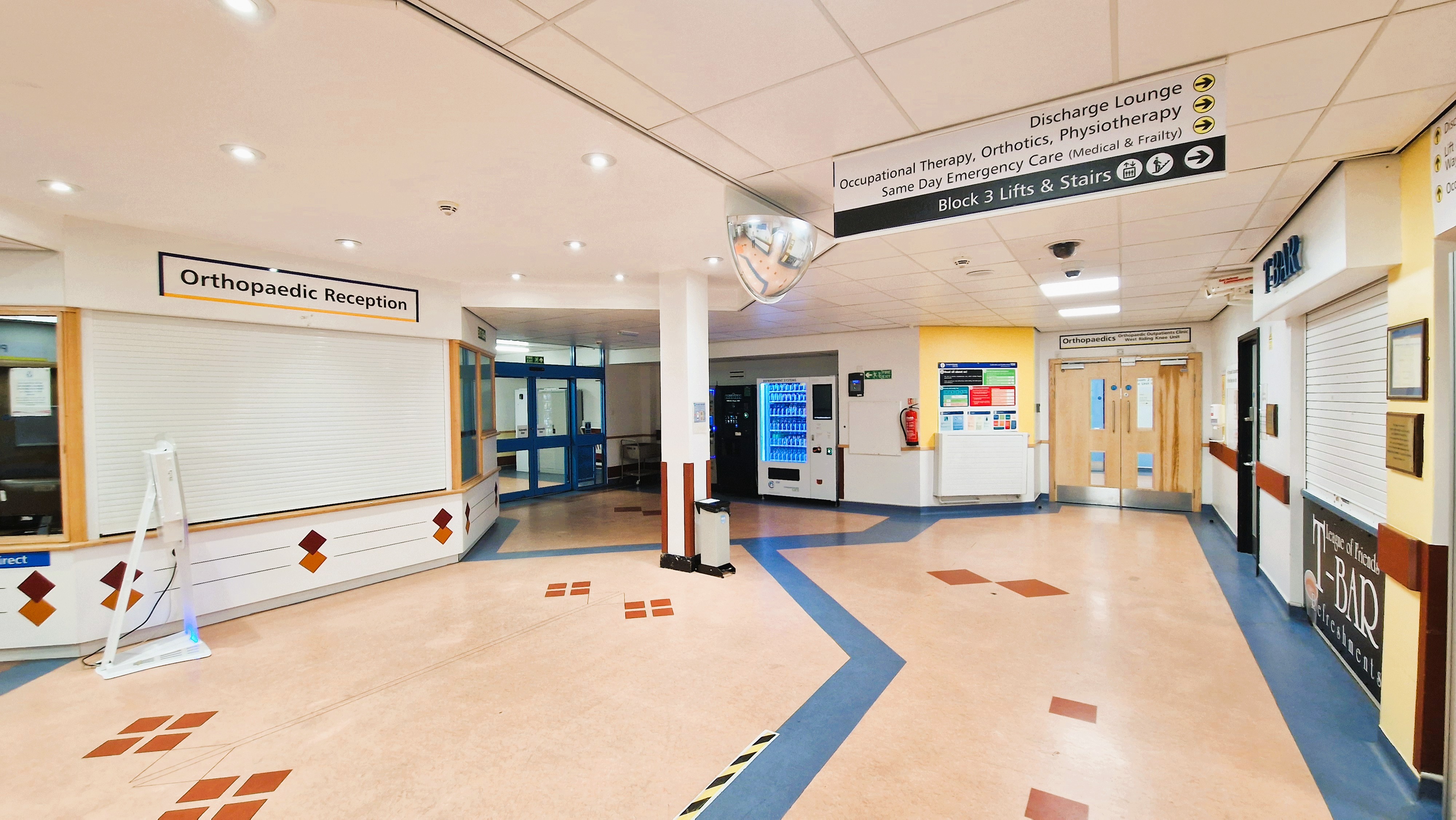 The orthopaedic reception leads onto a well-lit, large, clear, open hallway with a set of double doors and some automatic doors.
