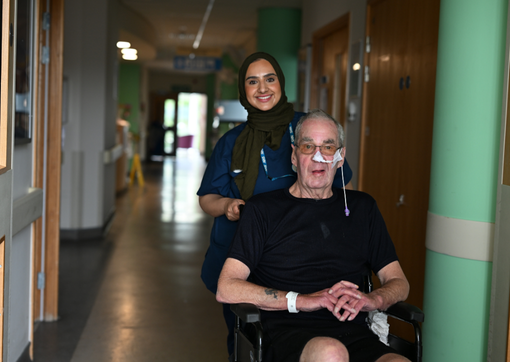 A nurse pushing a patient in a wheelchair on the stroke ward