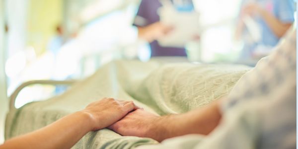 A patient in bed with a visitor holding their hand