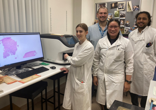 Some of our Cellular Pathology Team stood by the scanner and a digital screen showing large images of the scanned slide